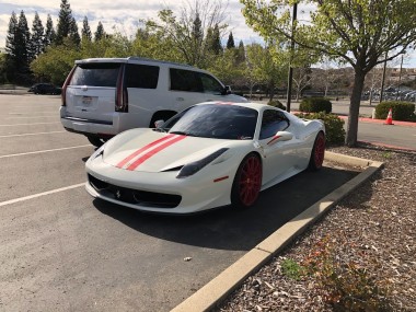 Picture of a white Ferrari 458 with red wheels and red racing stripes on the edge of a parking lot