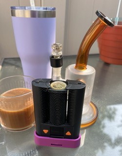 Coffee in a clear mug, purple insulated cup, orange clear bong with orange accents, mighty+ vaporizer, outside on glass patio table