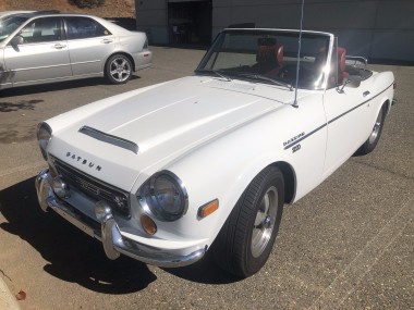 A white Datsun 2000 parked in front of an auto shop