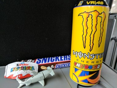 Kinder chocolate, hammerhead shark toy, Snickers candy bar, large yellow Monster Energy drink can.