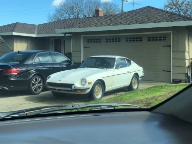 White Datsun 240z parked in a driveway next to a black BMW