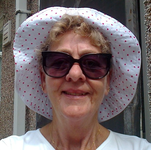 My mother looking happy, wearing big sunglasses and a white floppy hat with small pink spots.