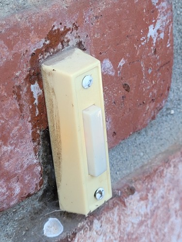 Plastic thing with lighted plastic button mounted on a brick gate post. Lighted plastic button does something when pressed, although no one under the age of 45 seems to comprehend this.