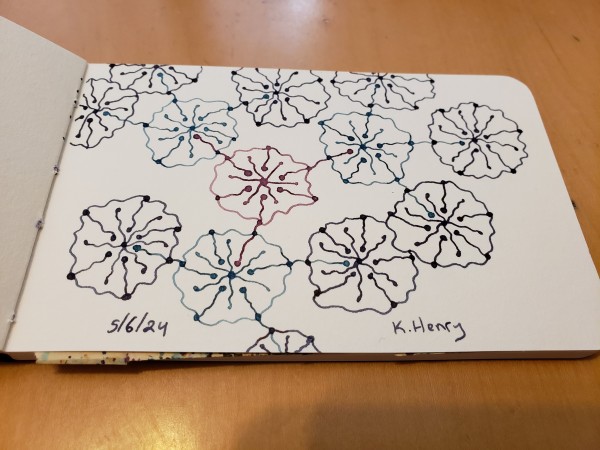 Hand drawn generative art in ink on an open page of my sketchbook. The abstract pattern looks a bit like something under a microscope or a network of flowers.