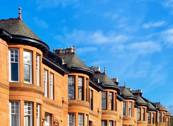 A row of red sandstone terraces houses, with distinctive bow windows, against an almost cloudless bkue sky.