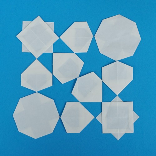 A blue square of paper with folded ten shapes attached that are folded from white paper. The white shapes come in three types: octagram (eight-pointed star that looks like two overlapping squares), regular octagon and irregular (but symmetrical) hexagon. The gaps between the white shapes form kites and five-pointed stars.