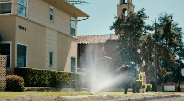 Boba Fett character getting hit by sprinklers near an apartment building and church