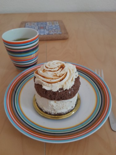 un gâteau mousseux rond dans une assiette à bandes colorées assortie à la tasse juste derrière. Tasse qui contient du matcha. 