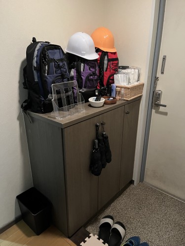 L’entrée d’un appartement japonais, avec trois sacs à dos (et deux casques) posés sur le meuble à chaussures, à côté de vide-poches et de masques. 