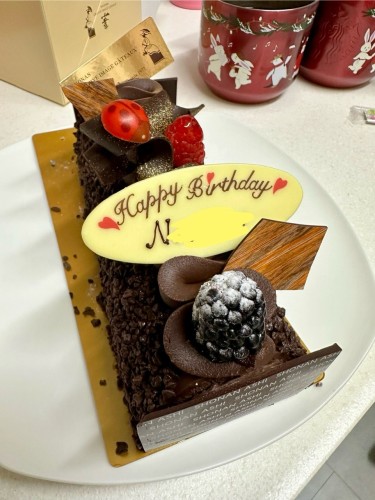 a long chocolate cake on a plate with blackberries and raspberries on top (and a chocolate ladybird), decorated with a nameplate made out of chocolate reading “happy birthday, N-“ with the rest of my daughter’s name censored 