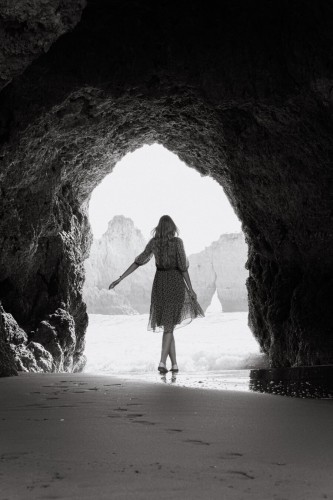 A woman walking towards the sea, cliffs surround her.