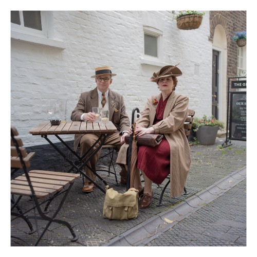 Portrait of a couple dressed in vintage clothing sitted at an outside pub table.