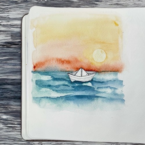 Aquarellmalerei eines Papierbootes auf dem Wasser mit einem Sonnenaufgang im Hintergrund, auf einem offenen Skizzenbuch.
