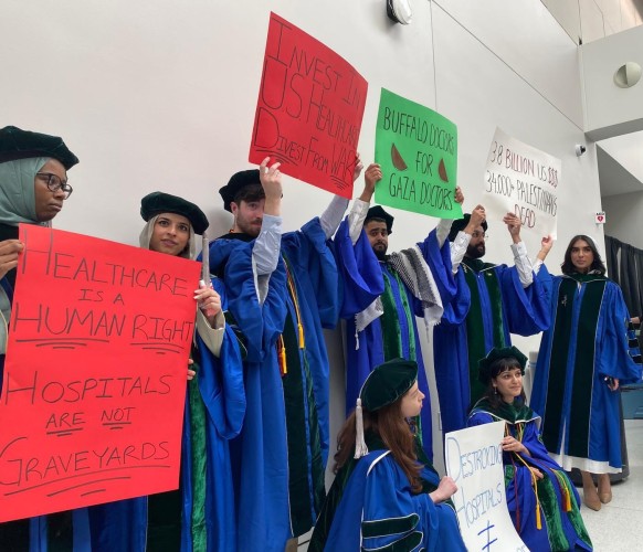 A group of newly qualified doctors in caps and gowns hold large placards reading
INVEST IN US HEALTHCARE, DIVEST FROM WAR
BUFFALO DOCTORS FOR GAZA DOCTORS
3.8 BILLION US $$$$ - 34,000+ PALESTINIAN DEAD
HEALTHCARE IS A HUMAN RIGHT
HOSPITALS ARE NOT GRAVEYARDS

