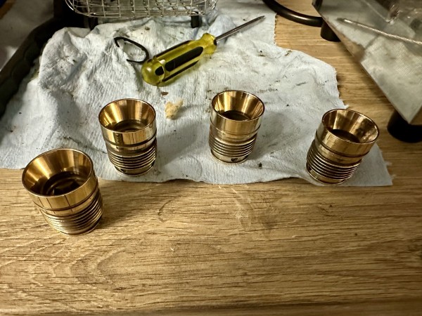 Four brass injector carriers sitting on a work surface, all pretty shiny