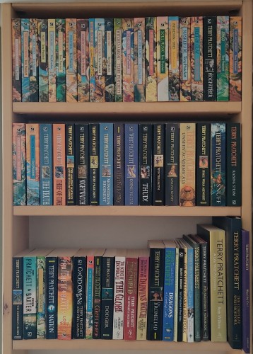 The same pile of Pratchett books now sorted on three shelves of the living room 'library'