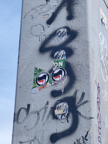 Photo d'un poteau. Un sticker de Mario Maréchal et Zemmour arraché, il reste leurs visages, recouvert chacun d'un sticker action antifasciste anarchiste. 