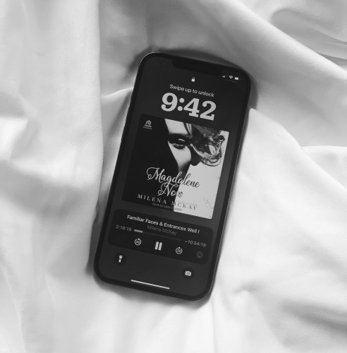 On white sheets, an iPhone with the audiobook of Magdalene Nox by Milena McKay, narrated by Abby Craden.