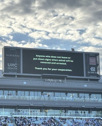 Above the stands at the football stadium the enormous announcement board reads
ANYONE WHO DOES NOT LEAVE OR PUT DOWN SIGNS WHEN ASKED WILL  BE REMOVED AND ARRESTED.
THANK YOU FOR YOUR COOPERATION.