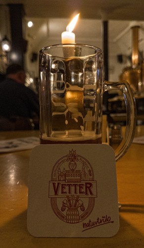A mostly drunk half litre of dunkel Hefeweizen beer brewed & served in Vetter near the Alte Brücke in Heidelberg. There is a Vetter beer mat propped up on the glass and a candle behind. The rest of the room is out of focus.