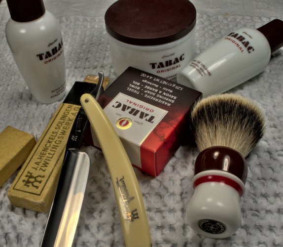 
A Stank Tank® refill surrounded by an empty Stank Tank® with matching splash, cologne and brush, and a big Friodur 14 straight razor