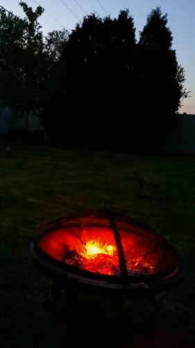 A firepit burns with a small evening fire at twilight.