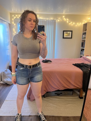 Me, a white woman with curly brown hair. I’m wearing a gray crop top and jean shorts. 