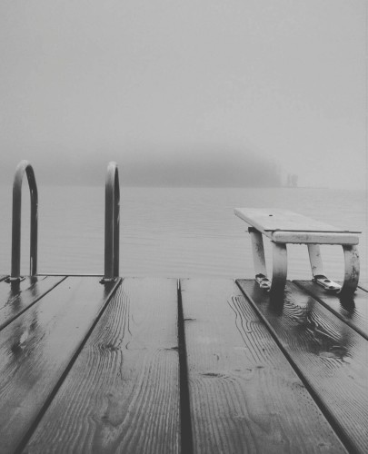 Dock with short diving plank & steel rails on ladder. Background is lake, in full fog