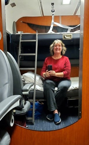 Sheila with Perceptive Travel on the Amtrak Coast Starlight train, in a bedroom compartment made up for bedtime. Two beds folded down, a small ladder to access the top one, Sheila sitting on lower bed taking photo from the compartment mirror.