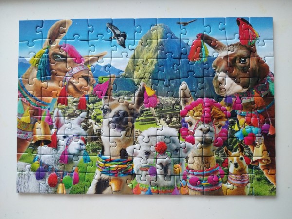 Photo of a small 99 piece jigsaw puzzle, showing a scene of the Matchu Pitchu temple ruins with 7 decorated llamas photoshopped on top.