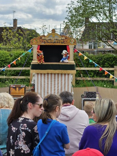 Punch & Judy show - a mini stage, with a striped canvas front. The audience, both children and adults, are sitting in front. Out of frame are the more subversive adults, laughing at the adult-level jokes.
