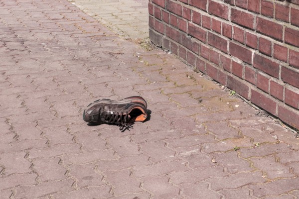 A brown shoe lying on the ground next to a brick wall.