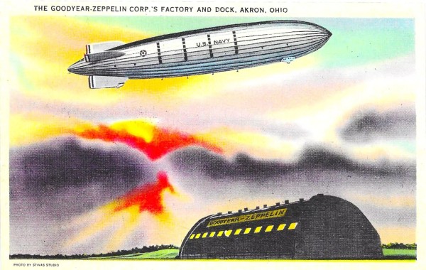 A large Dirigible is pointed up in the sky, while there is a fiery sun set in the background. Below is the hanger. 