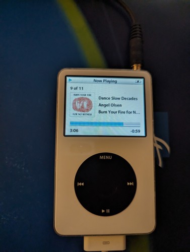 A white iPod classic 5.5 gen, with a black click wheel. It's playing angel olsen