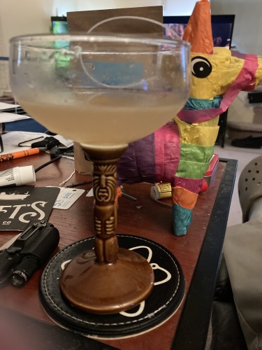 A delicious daiquiri in a tiki style cocktail coup glass and a mini piñata standing on the table behind it 
