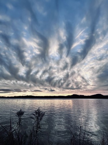 Dramatic clouds over a tranquil lake at dusk with silhouettes of shoreline vegetation.