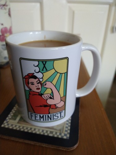 Mug of tea on a bedside cabinet, with an image of Rosie the riveter in red shirt and bandana 