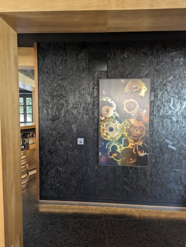 A view of the artwork on a vertical 55" display. The wall has a wood texture and is painted black.