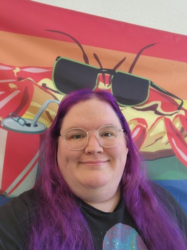 A white person with big round glasses and long purple hair, standing in front of a flag with a crab wearing sunglasses and sipping from a canned drink, over the gay pride stripes