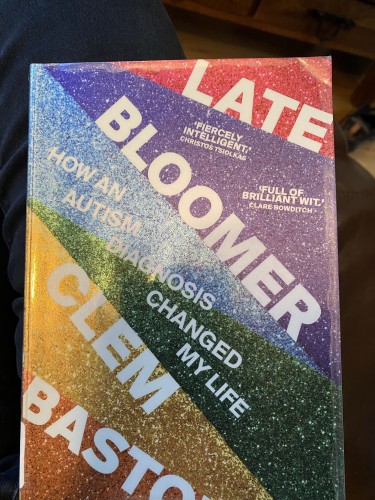 A book titled "Late Bloomer" by Clem Bastow, with a cover featuring diagonal rainbow glitter stripes and text about an autism diagnosis changing the author's life.