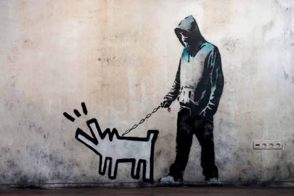 Banksy's grafitti art: a masked guy wearing a hoodie walking a dog. The dog is drawn in a visibly different style, with thick contour lines and sharp angles.