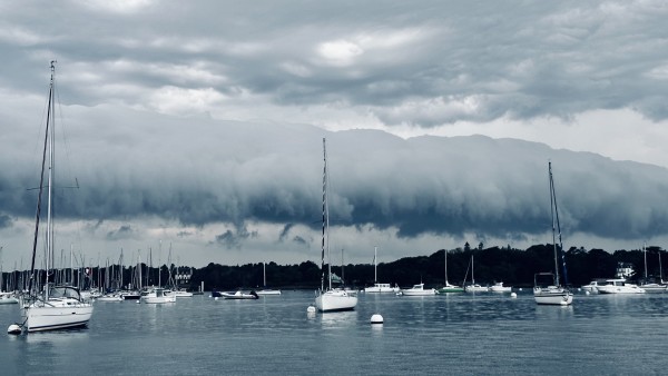 Voiliers amarrés sur des eaux calmes avec des nuages d’orage spectaculaires, groupés en ligne. 