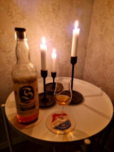 En flaska Springbank whisky och ett upphällt glas framför tre tända ljus på ett hörnbord.