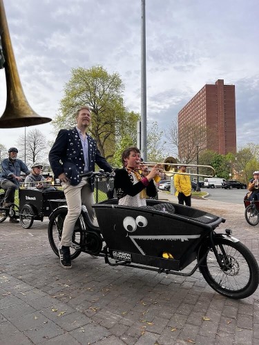 A black cargobike with chrome metal fenders (and there’s a lady playing a trombone sitting on the cargobox)