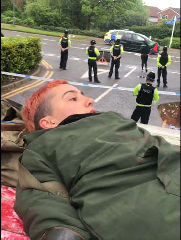Activist laying on the top of a van with a police cordon and line of officers in the background.