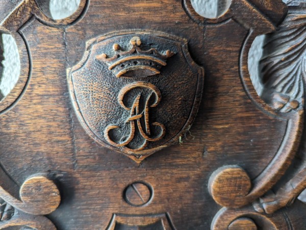 A cursive letter A intwined with a letter J with a crown above it, carved in wood.