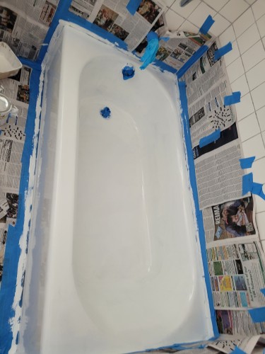 Bathtub surrounded by newspaper and taped off, bathtub has been coated with epoxy tub refinishing epoxy