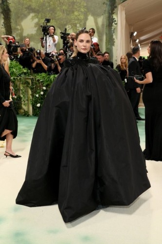 Photo of a woman dressed for the met gala. She has a large black cape covering her entire very puffy outfit.