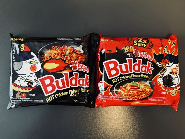 Two packs of Buldak Hot Chicken Ramen (vegan artifical flavored)

One black package with a fire spitting chicken on it and one red package with a concerned looking chicken with a bomb in its hand. At the top of the package stands "Two times spicy".