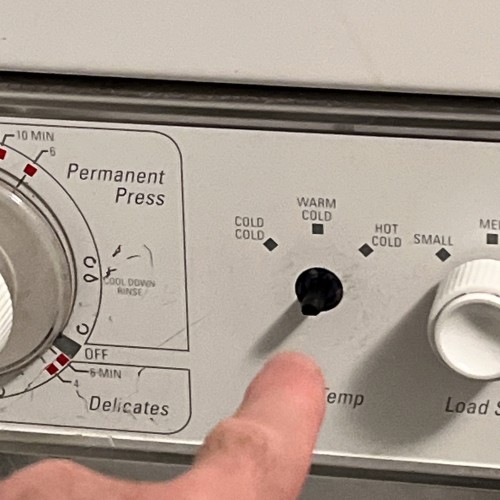 human finger pointing at the place where a knob to a washing machine used to be